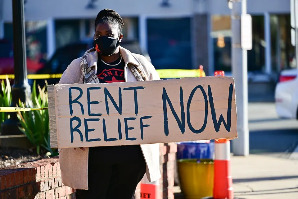 Person holding sign reading 'Rent Relief Now!' wearing blue face mask.